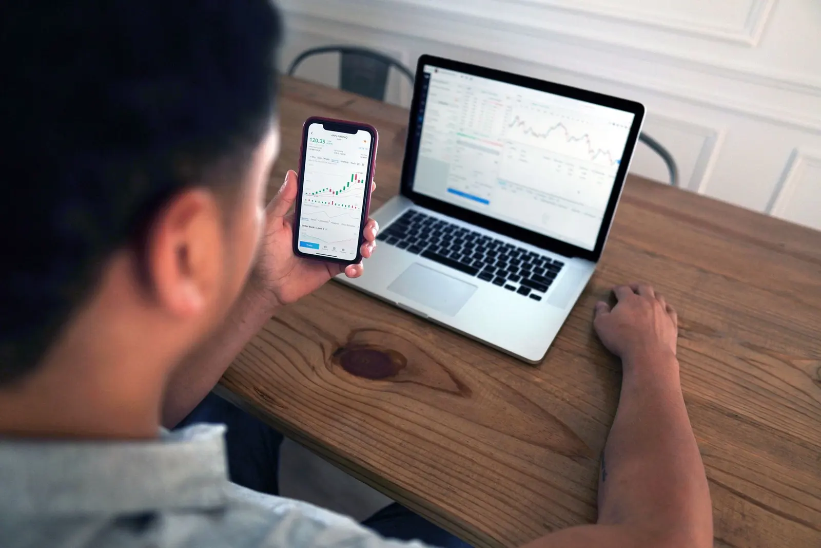 Person checking charges on a phone beside a laptop showing charts